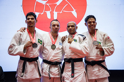 Quatro judocas posam sobre o lugar mais alto do pódio após a cerimônia de premiação. Da esquerda para a direita: o brasileiro Gabriel F. Rodrigues, medalha de prata, segura sua medalha e sorri para a câmera; ao seu lado está o argentino Eduardo Gauto, campeão da categoria, com a medalha de ouro no peito; em seguida aparece o brasileiro Deyverson de Souza, um dos medalhistas de bronze; e, à direita, o brasileiro Elielton de Oliveira, também medalhista de bronze, exibindo sua medalha com um sorris